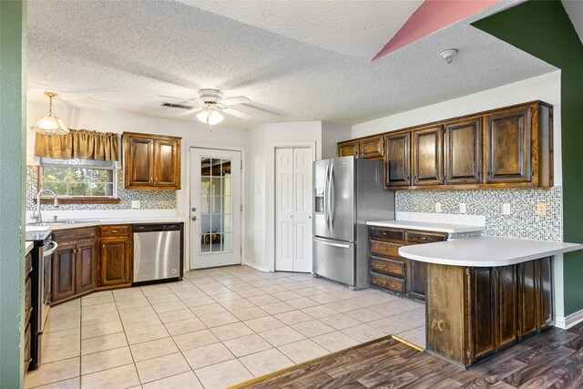 kitchen with sink, appliances with stainless steel finishes, kitchen peninsula, pendant lighting, and backsplash