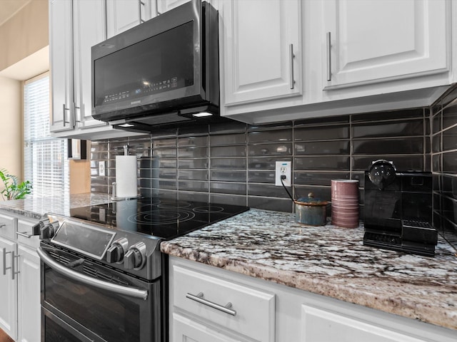 kitchen with range with two ovens, white cabinetry, backsplash, and light stone counters