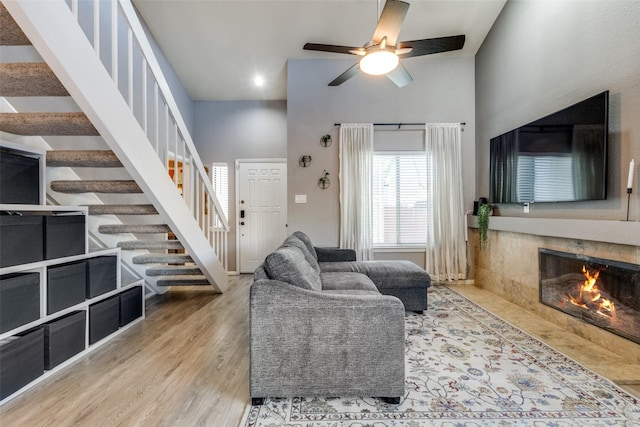 living room with ceiling fan, light wood-type flooring, a fireplace, and a towering ceiling