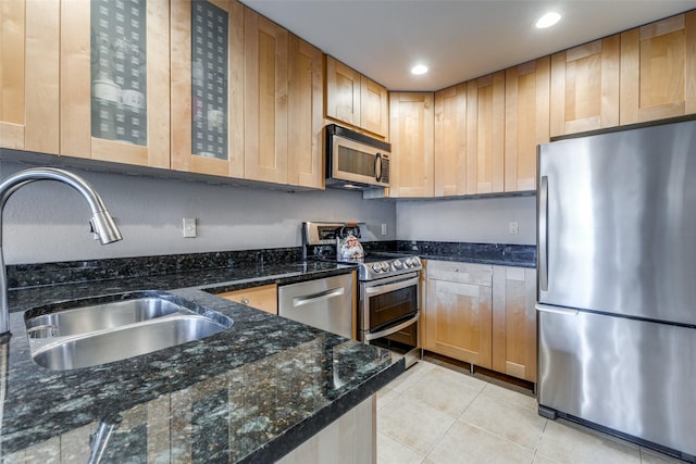 kitchen featuring appliances with stainless steel finishes, sink, dark stone countertops, and light tile patterned floors