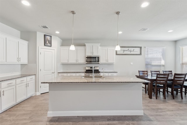 kitchen featuring decorative light fixtures, a center island with sink, white cabinets, and appliances with stainless steel finishes