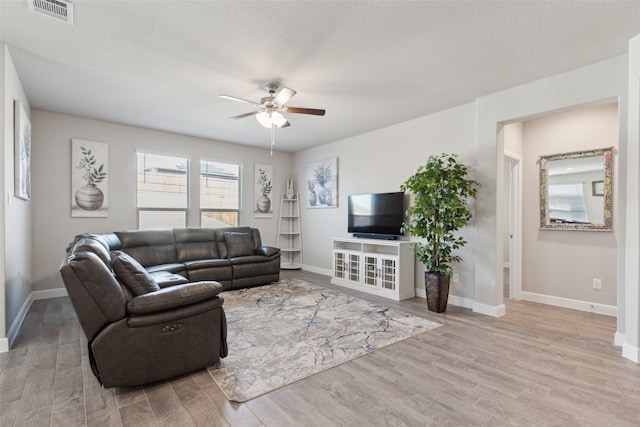 living room with ceiling fan, a textured ceiling, and light wood-type flooring