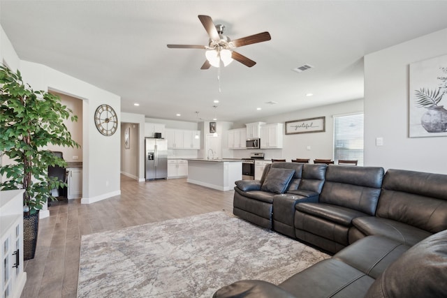 living room featuring ceiling fan, sink, and light wood-type flooring