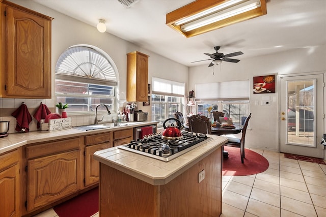 kitchen featuring stainless steel gas stovetop, tile countertops, sink, and light tile patterned floors