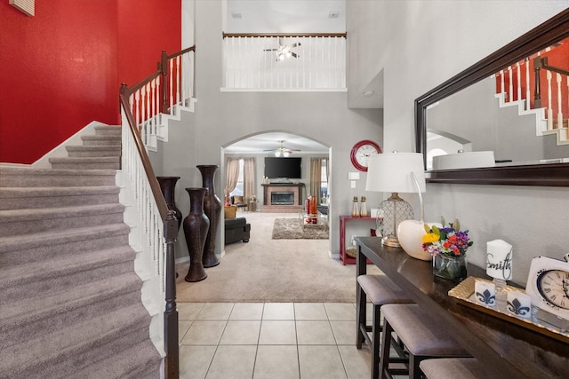 entryway featuring a towering ceiling, light colored carpet, and ceiling fan