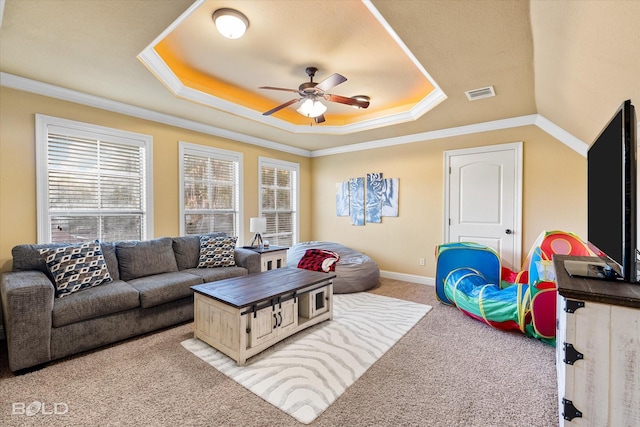 carpeted living room with a raised ceiling, ornamental molding, and ceiling fan