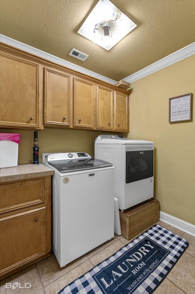 washroom featuring cabinets, a textured ceiling, light tile patterned floors, ornamental molding, and washer and clothes dryer