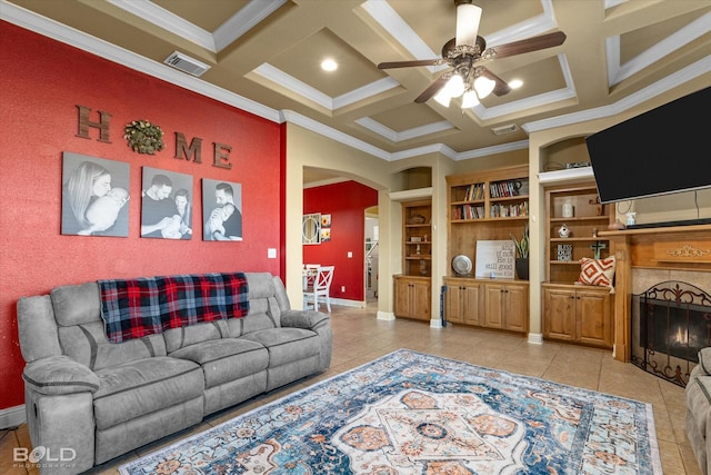 tiled living room with built in features, ceiling fan, coffered ceiling, ornamental molding, and beamed ceiling