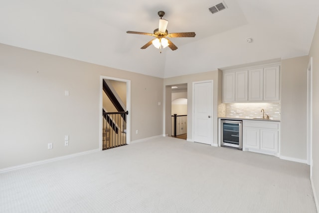 unfurnished living room with sink, ceiling fan, vaulted ceiling, light colored carpet, and beverage cooler