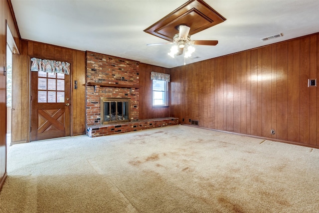 unfurnished living room featuring a brick fireplace, wood walls, ceiling fan, and carpet flooring