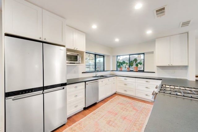 kitchen with white cabinetry, sink, backsplash, stainless steel appliances, and light wood-type flooring