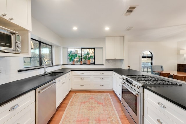 kitchen featuring sink, appliances with stainless steel finishes, white cabinetry, kitchen peninsula, and light wood-type flooring