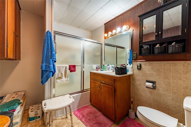 full bathroom with vanity, toilet, combined bath / shower with glass door, and tile walls