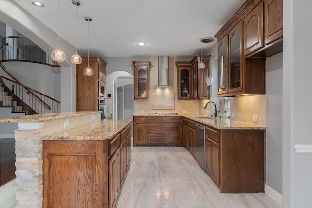 kitchen with appliances with stainless steel finishes, tasteful backsplash, sink, hanging light fixtures, and wall chimney range hood