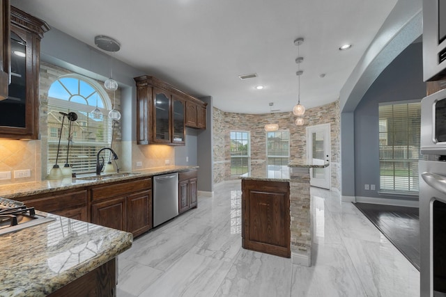 kitchen with pendant lighting, sink, backsplash, stainless steel dishwasher, and light stone counters