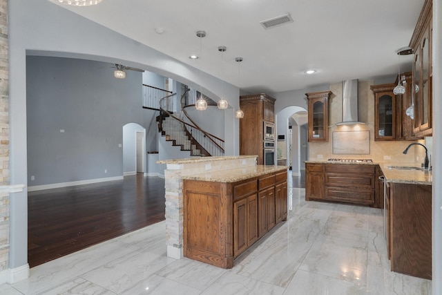 kitchen featuring wall chimney exhaust hood, sink, hanging light fixtures, a kitchen island, and stainless steel appliances