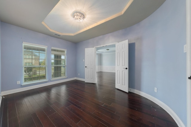 unfurnished bedroom featuring a tray ceiling and dark hardwood / wood-style floors