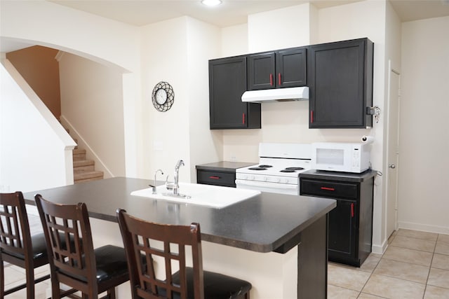 kitchen featuring light tile patterned flooring, white appliances, dark countertops, under cabinet range hood, and a sink