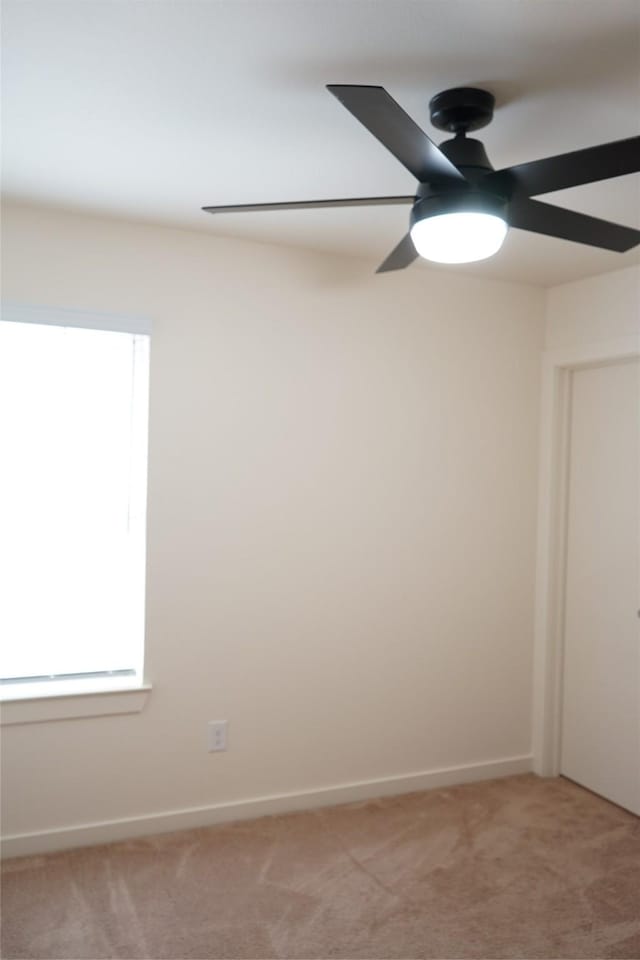 spare room featuring a ceiling fan, light carpet, and baseboards