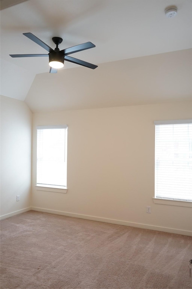 spare room with light colored carpet, vaulted ceiling, baseboards, and a ceiling fan
