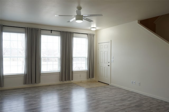 spare room featuring a ceiling fan, baseboards, a healthy amount of sunlight, and wood finished floors