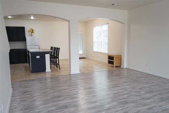 kitchen featuring a breakfast bar, a center island with sink, arched walkways, open floor plan, and freestanding refrigerator