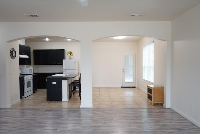 kitchen featuring a kitchen breakfast bar, white appliances, a sink, visible vents, and dark cabinets