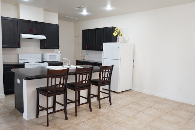 kitchen with a kitchen breakfast bar, under cabinet range hood, white appliances, visible vents, and dark cabinets