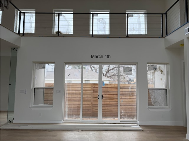 interior space featuring a healthy amount of sunlight, baseboards, a towering ceiling, and wood finished floors