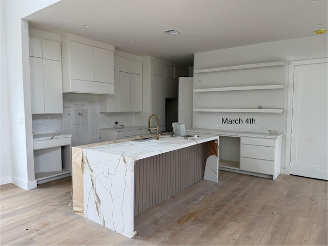 kitchen featuring open shelves, modern cabinets, a kitchen island with sink, and light wood finished floors