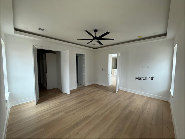 unfurnished bedroom with visible vents, a raised ceiling, light wood-type flooring, and baseboards