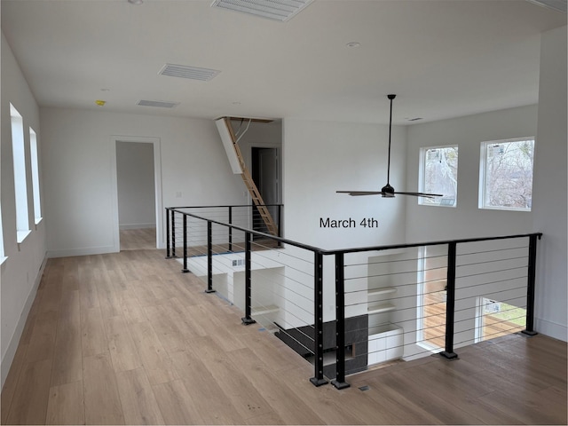 hallway with an upstairs landing, wood finished floors, visible vents, and baseboards