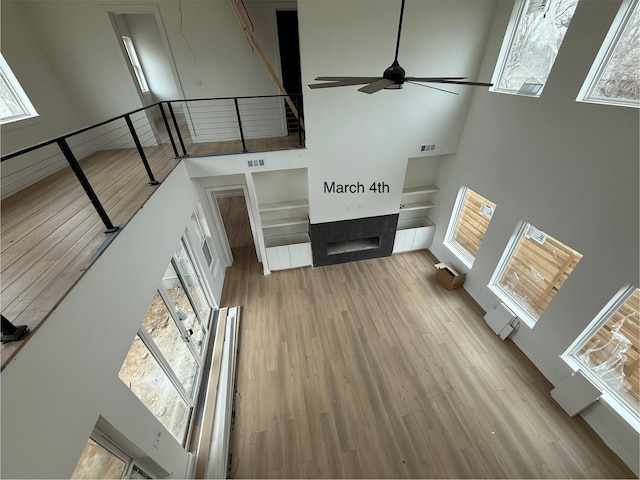 unfurnished living room featuring visible vents, a fireplace, a high ceiling, and wood finished floors