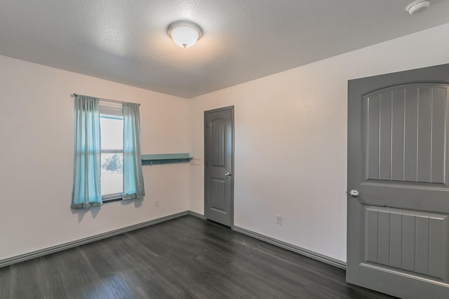 unfurnished bedroom with a textured ceiling, dark wood-type flooring, and baseboards