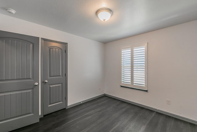 unfurnished bedroom featuring dark wood-style floors, a textured ceiling, and baseboards