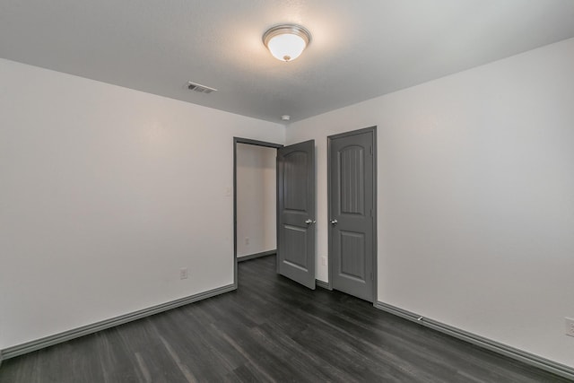 empty room featuring baseboards, visible vents, and dark wood-style flooring