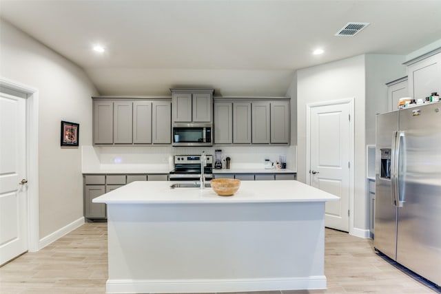 kitchen with tasteful backsplash, stainless steel appliances, gray cabinets, and an island with sink