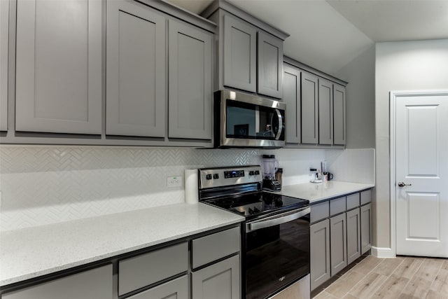 kitchen featuring light stone counters, backsplash, gray cabinets, and appliances with stainless steel finishes