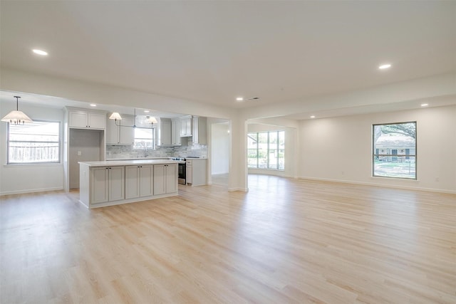 kitchen featuring electric stove, backsplash, hanging light fixtures, a center island, and light hardwood / wood-style flooring