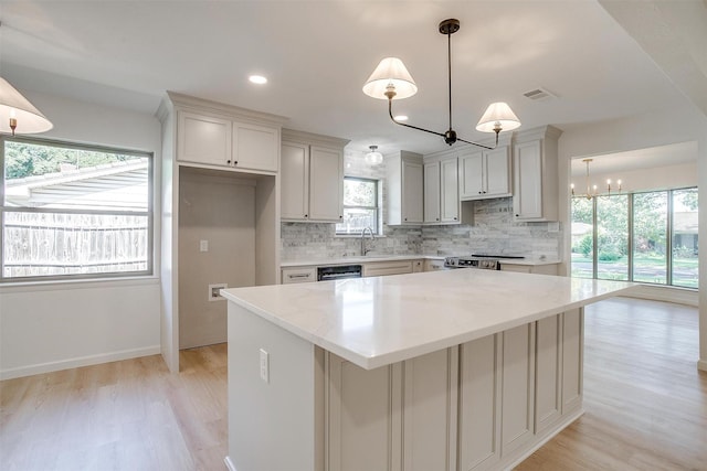 kitchen featuring a kitchen island, tasteful backsplash, sink, hanging light fixtures, and light stone counters