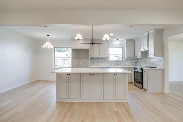 kitchen with sink, hanging light fixtures, a kitchen island, electric stove, and light hardwood / wood-style floors