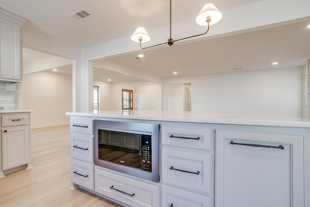 kitchen with light hardwood / wood-style flooring, black microwave, white cabinets, decorative backsplash, and decorative light fixtures