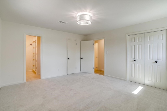 unfurnished bedroom with light colored carpet, ensuite bathroom, and a closet