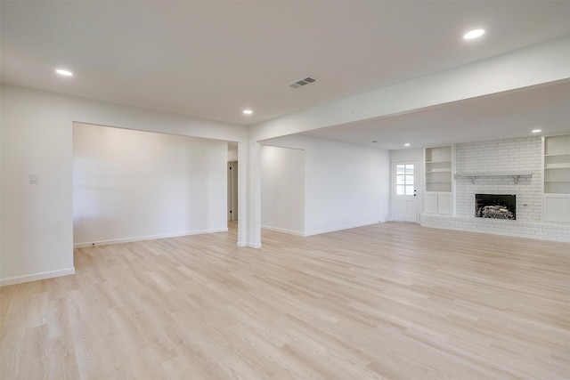 unfurnished living room featuring a brick fireplace, light hardwood / wood-style flooring, and built in shelves