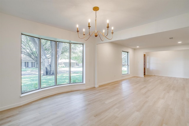 unfurnished room featuring an inviting chandelier, a healthy amount of sunlight, and light wood-type flooring