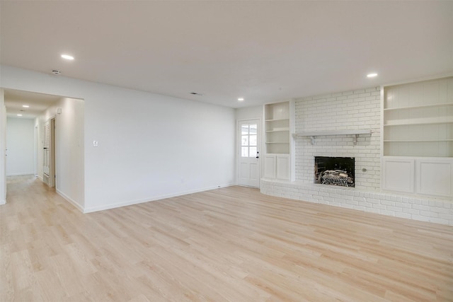 unfurnished living room featuring a brick fireplace, light hardwood / wood-style flooring, and built in shelves