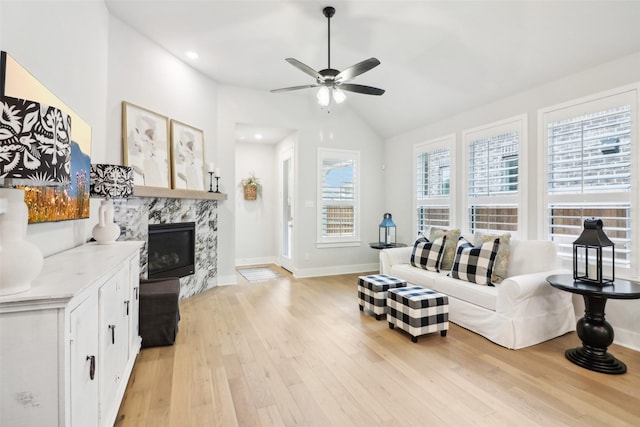 living room with a high end fireplace, vaulted ceiling, light hardwood / wood-style floors, and ceiling fan