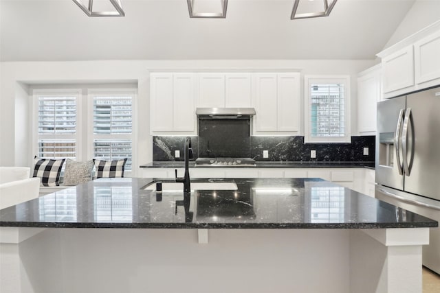 kitchen with a kitchen island with sink, dark stone countertops, stainless steel appliances, tasteful backsplash, and white cabinets