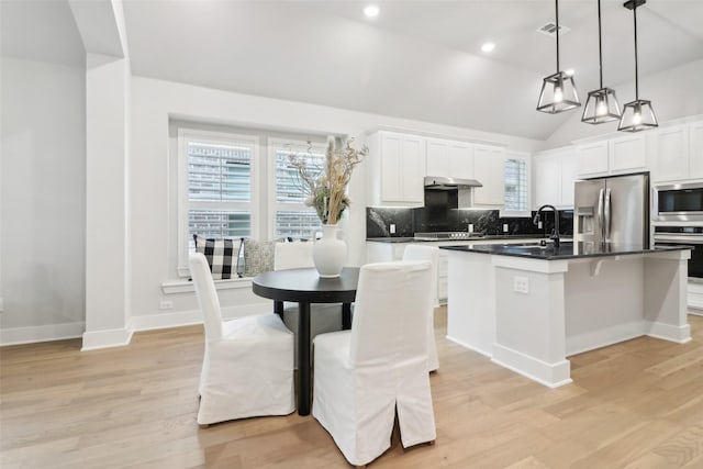 kitchen with pendant lighting, appliances with stainless steel finishes, white cabinets, a center island with sink, and decorative backsplash