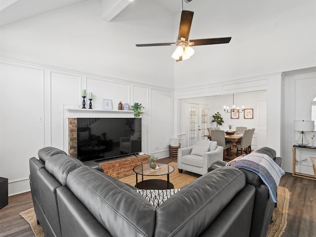 living room with dark wood-type flooring, ceiling fan with notable chandelier, high vaulted ceiling, and a brick fireplace